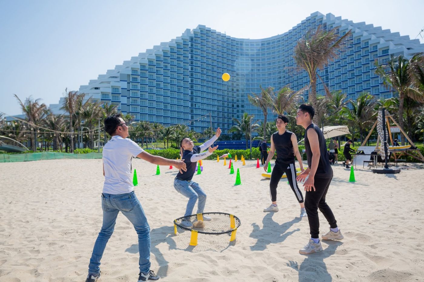 Friends playing a ball game on the sand in front of the wave-shaped tower