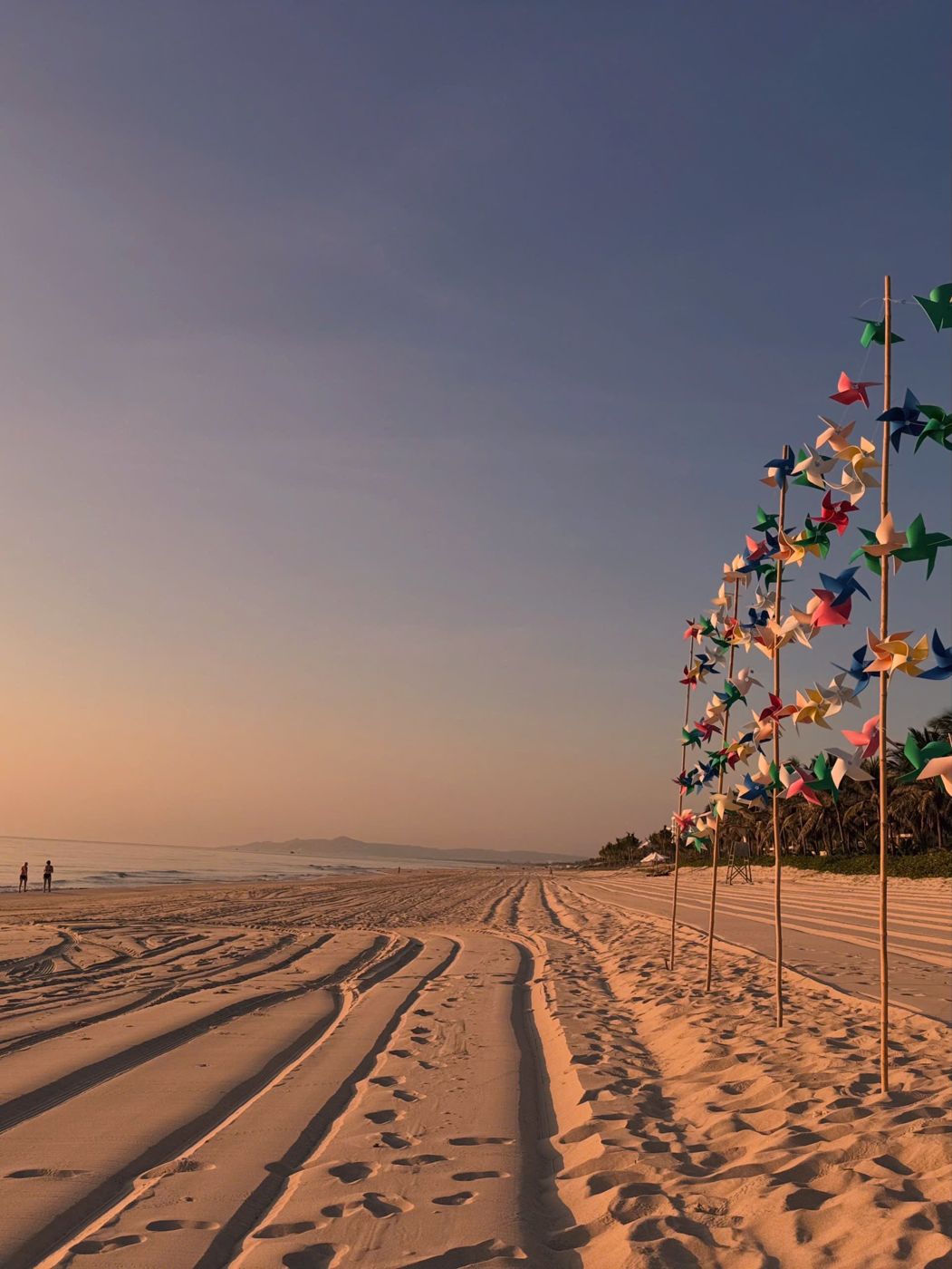 Rows of colourful pinwheels on the sand under a pink dawn sky