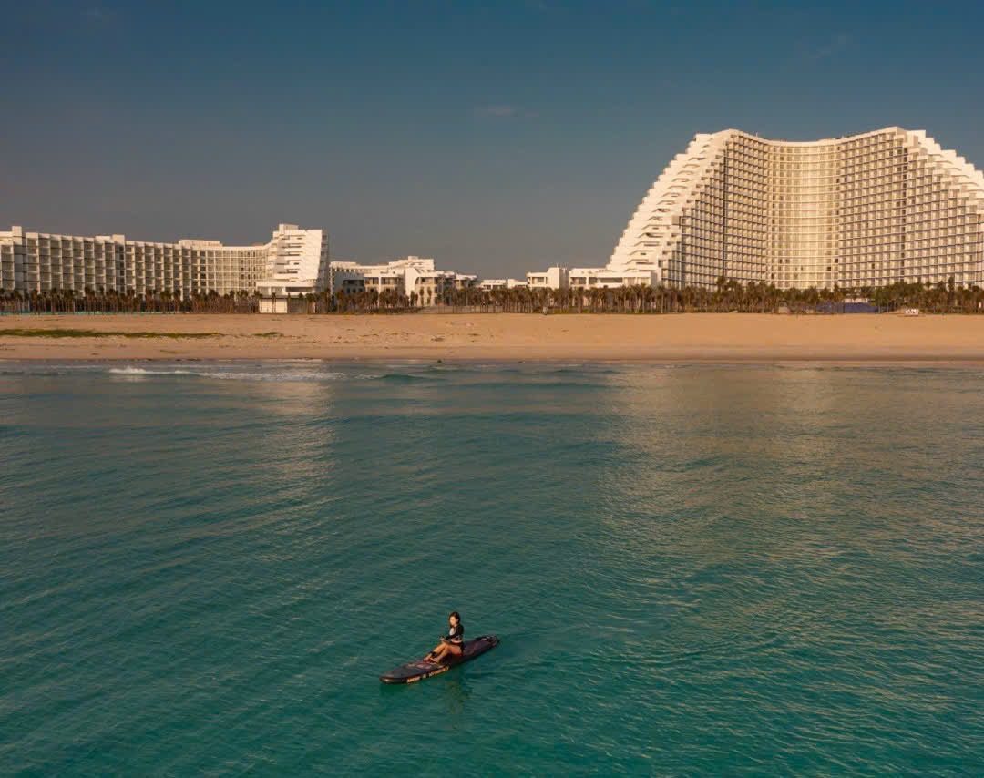 Paddleboarder on turquoise water in front of the wave-shaped resort building